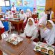 Anak-anak sekolah dasar menikmati makan bergizi gratis bersama di ruang kelas sederhana di daerah terpencil Indonesia.