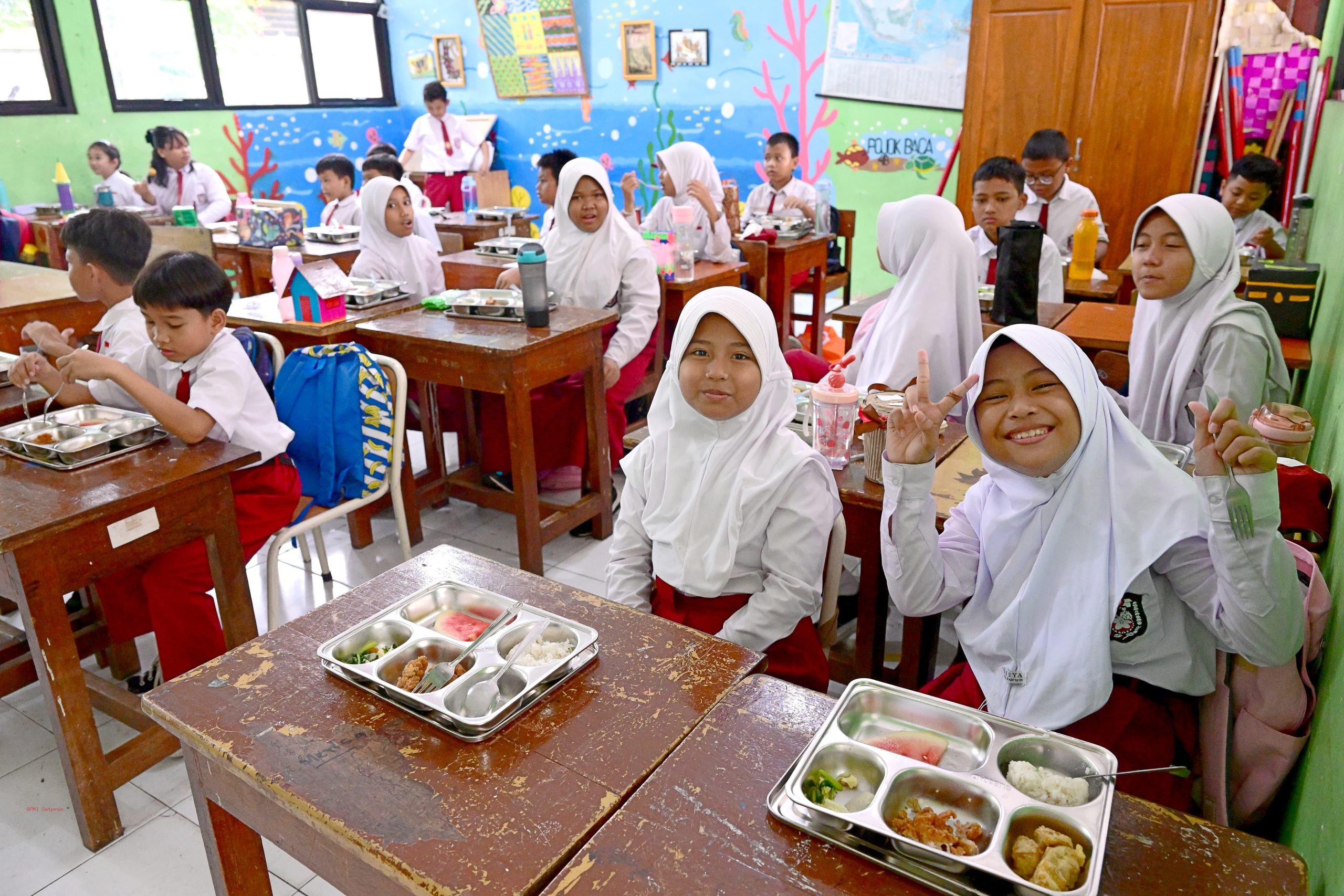 Anak-anak sekolah dasar menikmati makan bergizi gratis bersama di ruang kelas sederhana di daerah terpencil Indonesia.