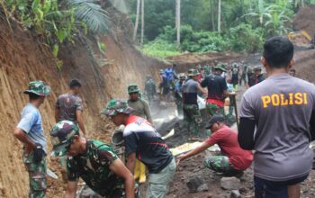 Personel Satgas TMMD Kodim 1309/Manado tetap bekerja di tengah hujan, menuntaskan pengancing badan jalan sepanjang 780 meter bersama warga.
