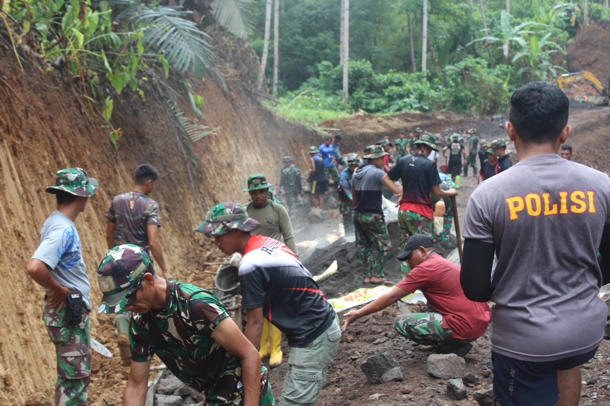 Personel Satgas TMMD Kodim 1309/Manado tetap bekerja di tengah hujan, menuntaskan pengancing badan jalan sepanjang 780 meter bersama warga.